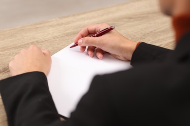 Photo of Writer signing autograph in book at wooden table indoors, closeup