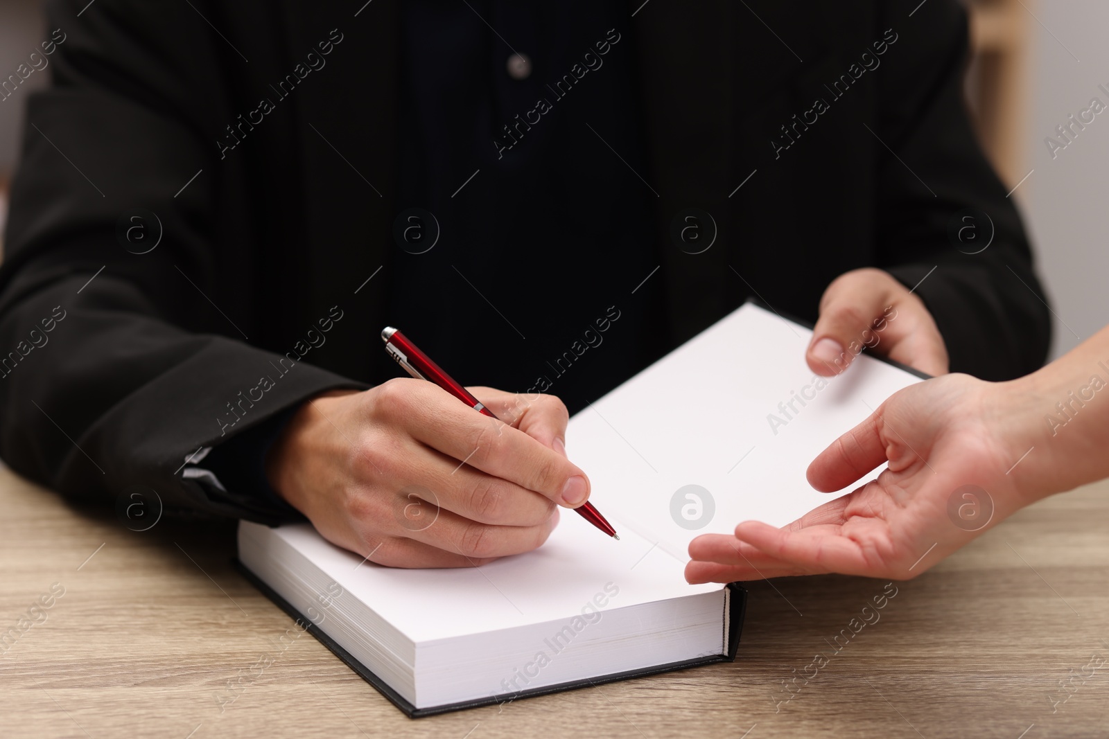 Photo of Writer signing autograph in book at wooden table indoors, closeup