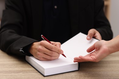 Photo of Writer signing autograph in book at wooden table indoors, closeup