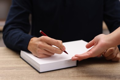 Photo of Writer signing autograph in book at wooden table indoors, closeup