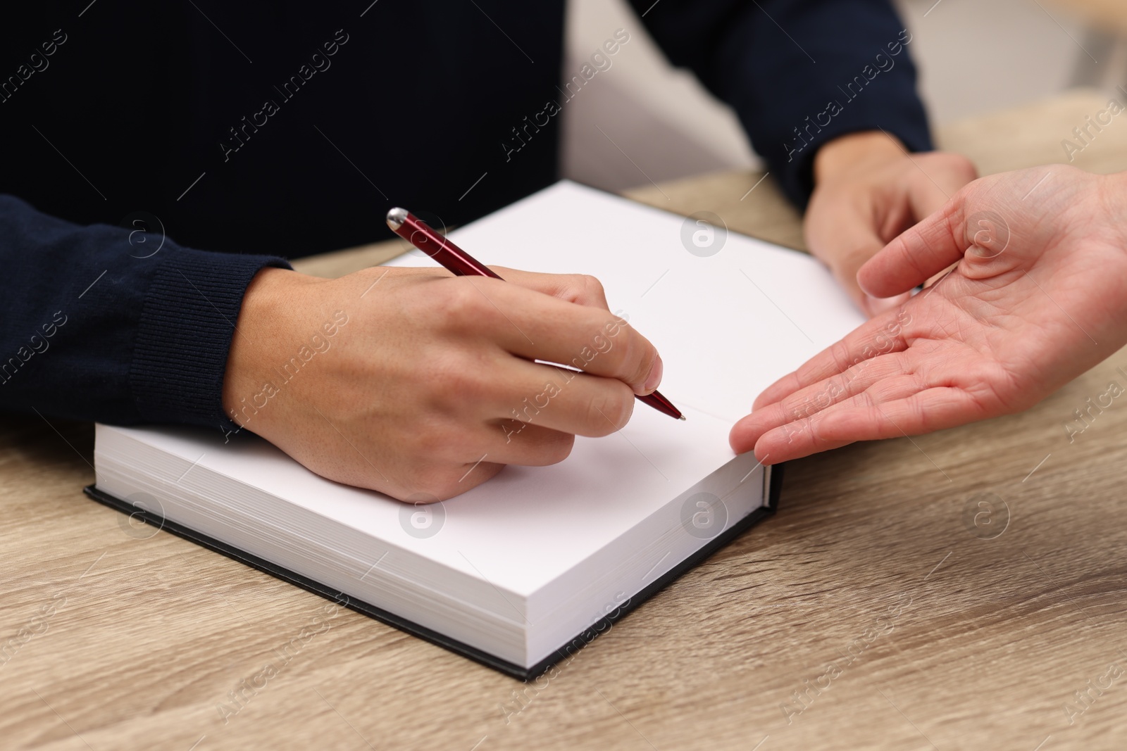 Photo of Writer signing autograph in book at wooden table indoors, closeup