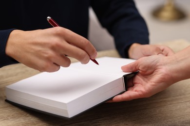 Photo of Writer signing autograph in book at wooden table indoors, closeup