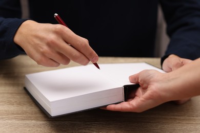 Photo of Writer signing autograph in book at wooden table indoors, closeup