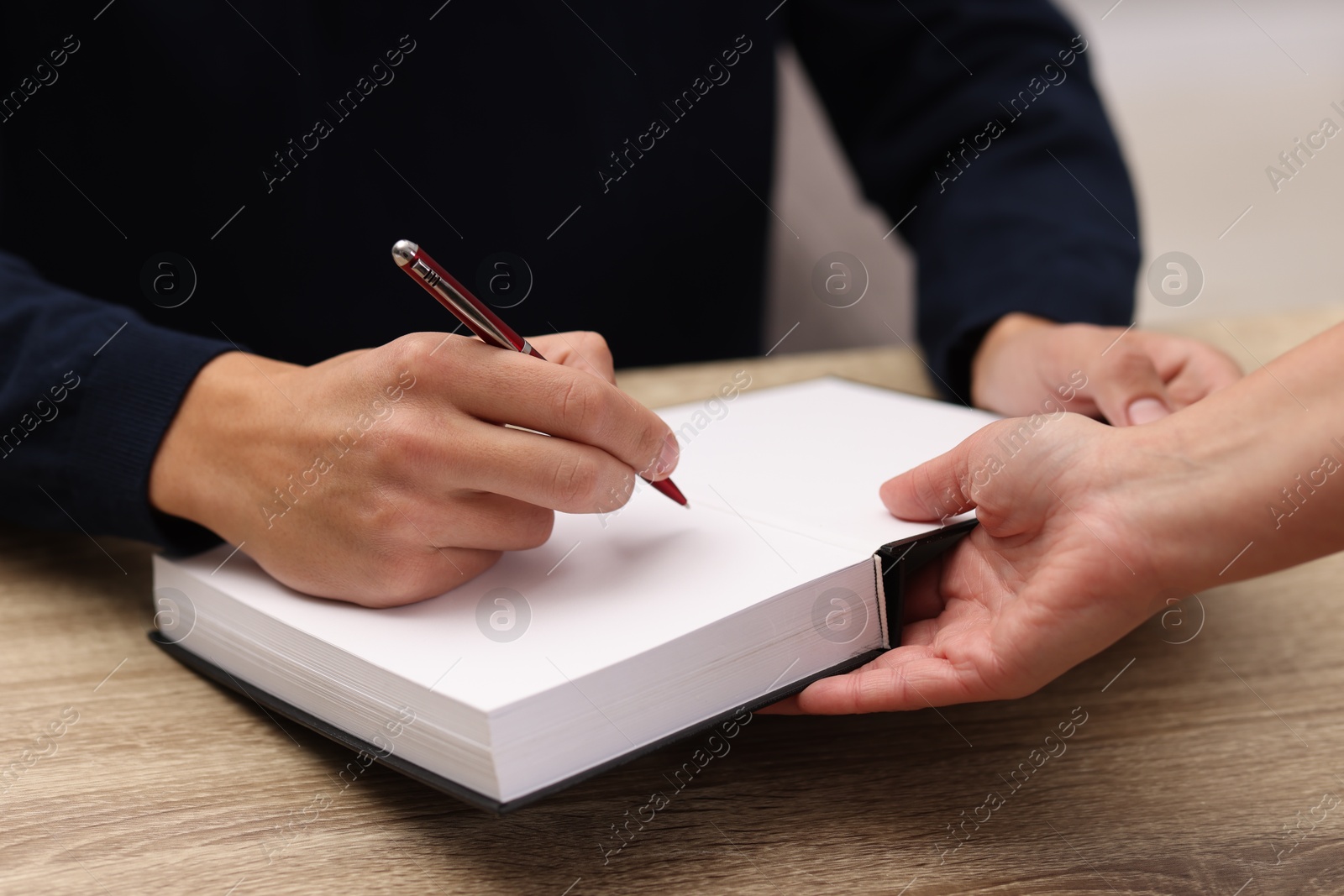 Photo of Writer signing autograph in book at wooden table indoors, closeup