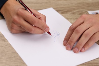 Photo of Writer signing autograph on sheet of paper at wooden table, closeup