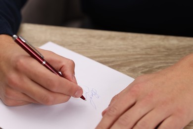 Photo of Writer signing autograph on sheet of paper at wooden table, closeup