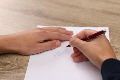 Writer signing autograph on sheet of paper at wooden table, closeup