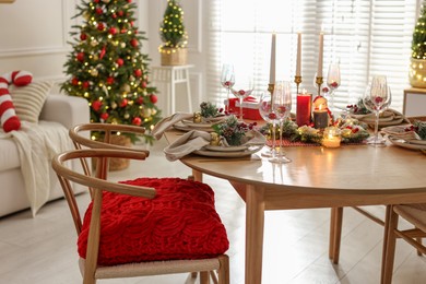 Photo of Christmas table setting with stylish dishware, glasses and burning candles in festive decorated room