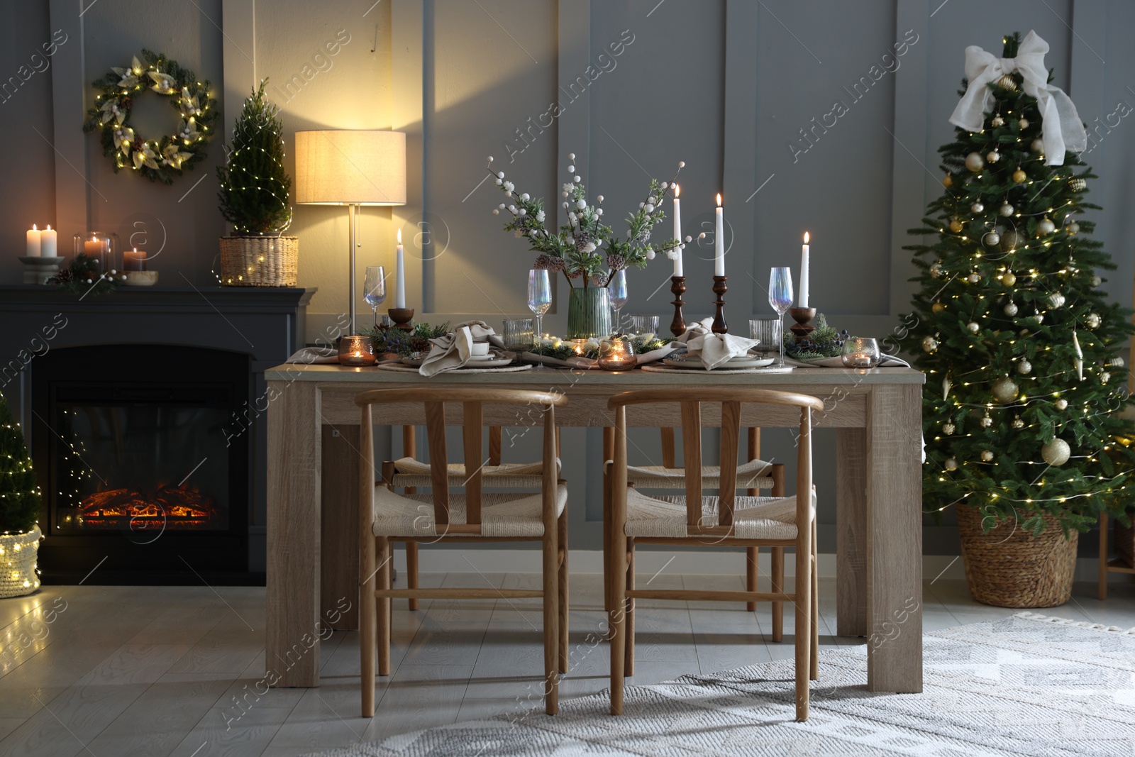 Photo of Christmas table setting with stylish dishware, glasses and burning candles in festive decorated room