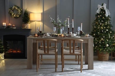 Photo of Christmas table setting with stylish dishware, glasses and burning candles in festive decorated room