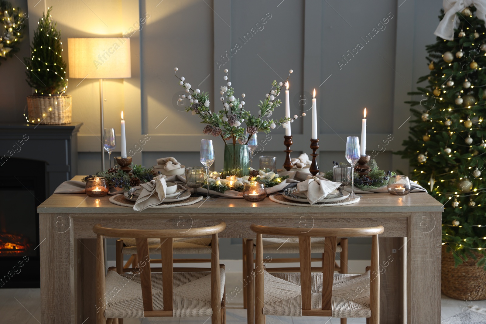 Photo of Christmas table setting with stylish dishware, glasses and burning candles in festive decorated room