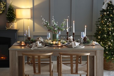 Photo of Christmas table setting with stylish dishware, glasses and burning candles in festive decorated room