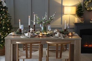 Photo of Christmas table setting with stylish dishware, glasses and burning candles in festive decorated room