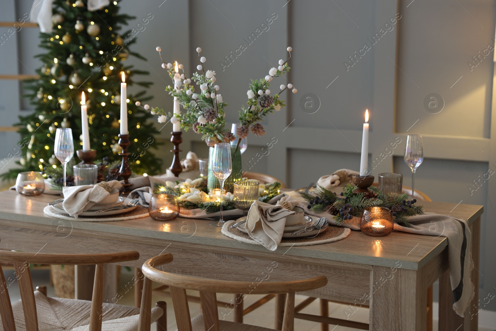 Photo of Christmas table setting with stylish dishware, glasses and burning candles in festive decorated room