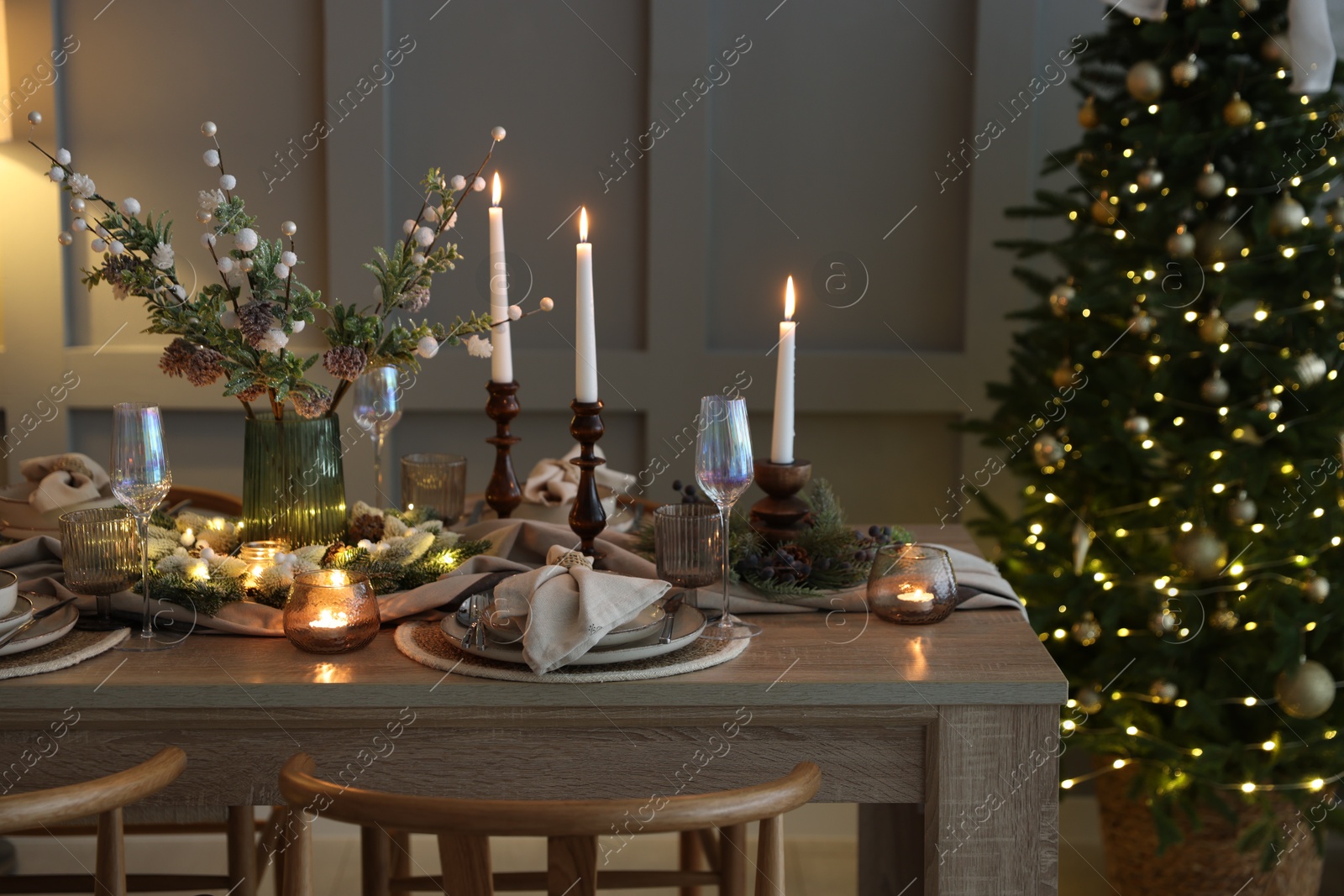 Photo of Christmas table setting with stylish dishware, glasses and burning candles in festive decorated room