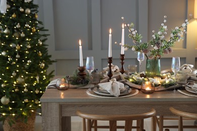 Photo of Christmas table setting with stylish dishware, glasses and burning candles in festive decorated room