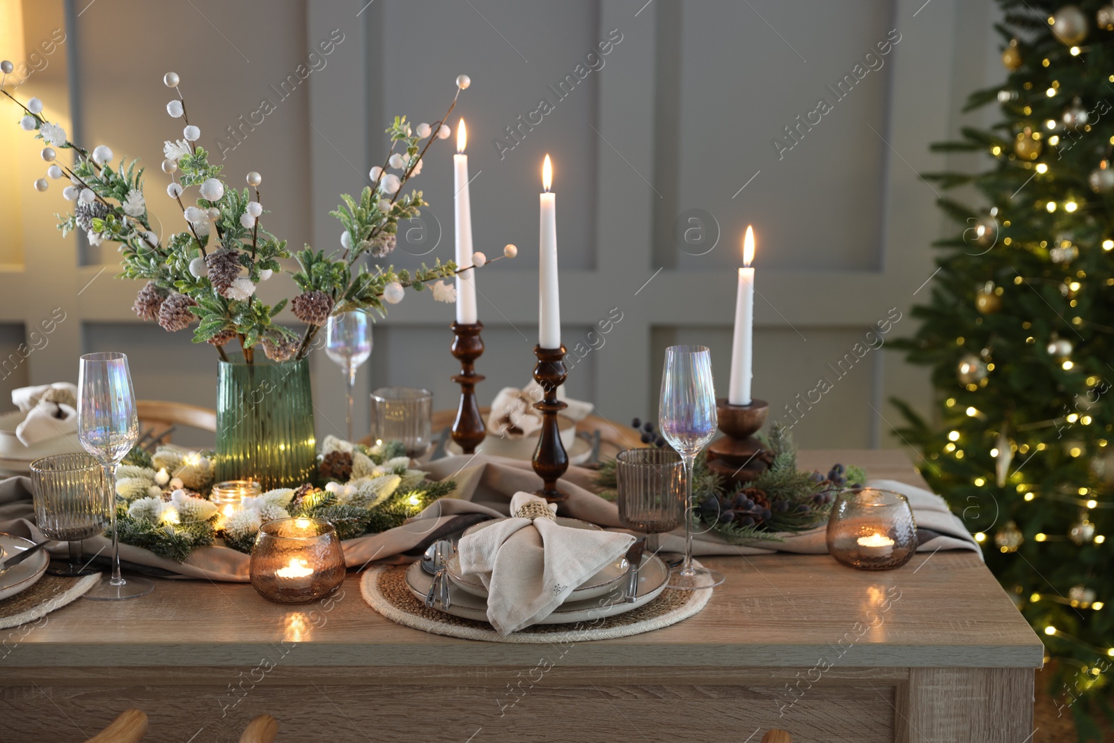 Photo of Christmas table setting with stylish dishware, glasses and burning candles in festive decorated room