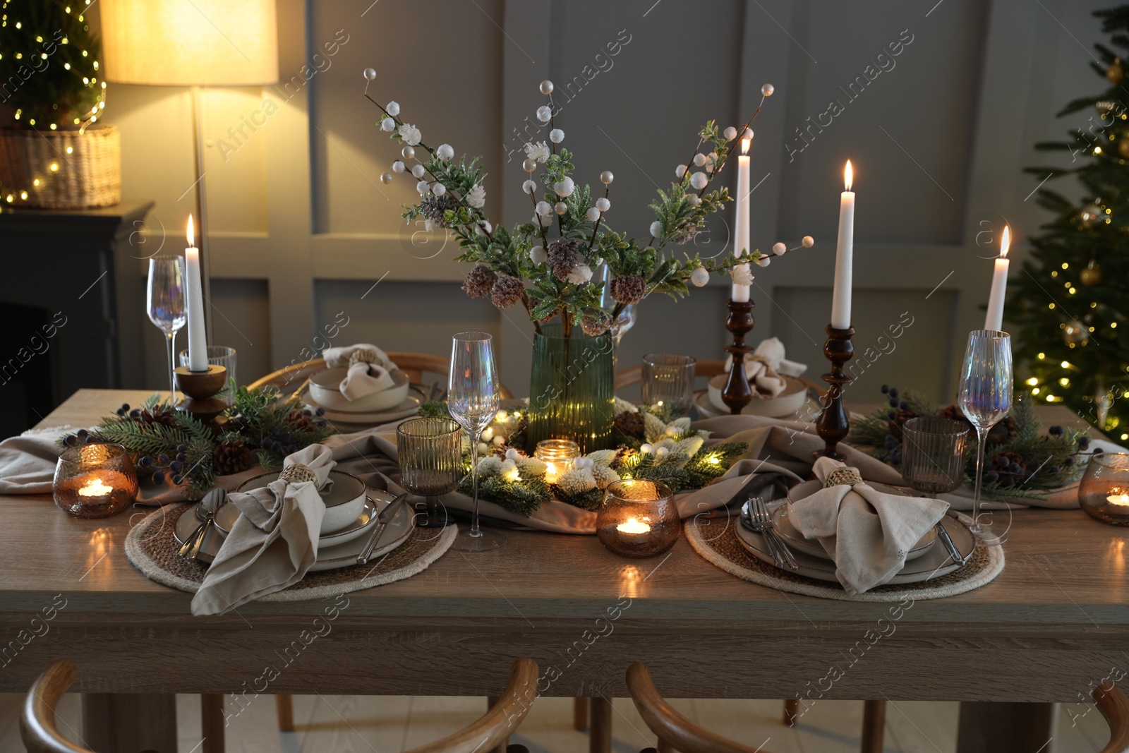 Photo of Christmas table setting with stylish dishware, glasses and burning candles in festive decorated room