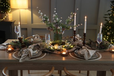 Photo of Christmas table setting with stylish dishware, glasses and burning candles in festive decorated room