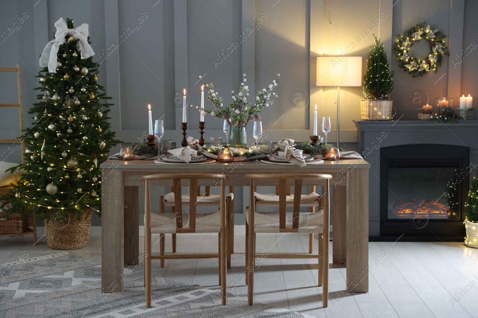 Photo of Christmas table setting with stylish dishware, glasses and burning candles in festive decorated room