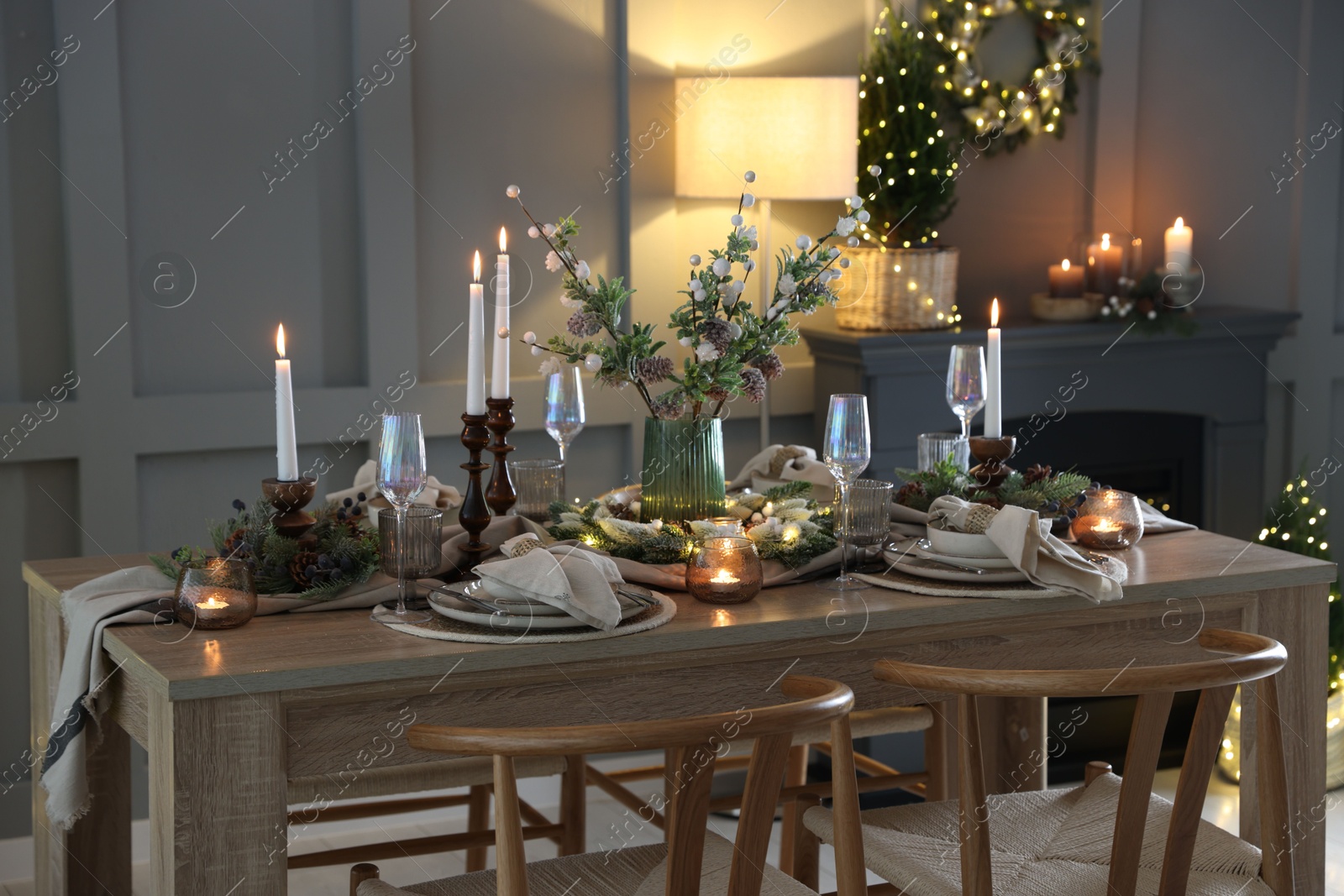 Photo of Christmas table setting with stylish dishware, glasses and burning candles in festive decorated room