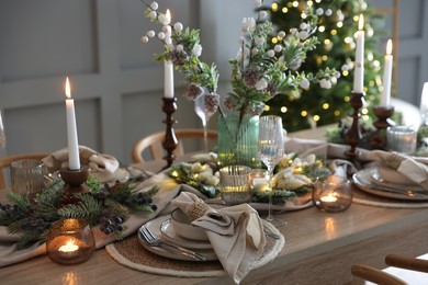 Photo of Christmas celebration. Festive table setting with dishware, glasses and decor in room