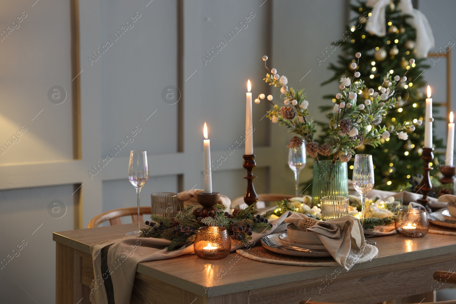 Photo of Christmas table setting with stylish dishware, glasses and burning candles in festive decorated room