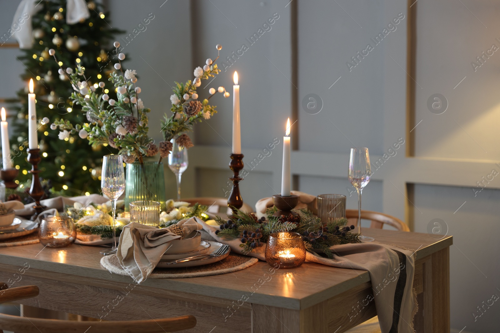 Photo of Christmas table setting with stylish dishware, glasses and burning candles in festive decorated room