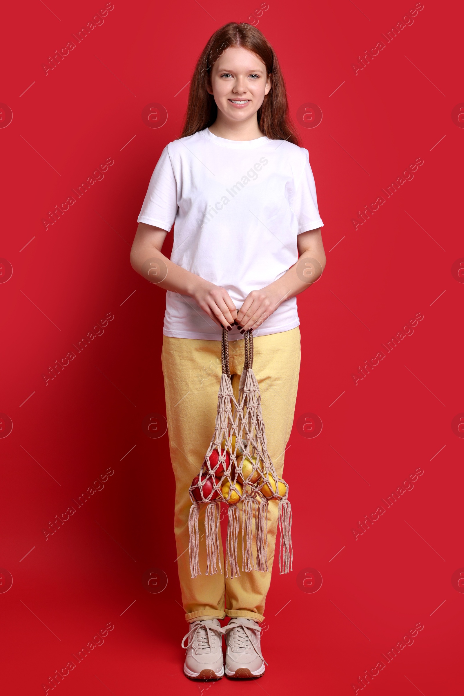 Photo of Teenage girl with handmade macrame bag on red background