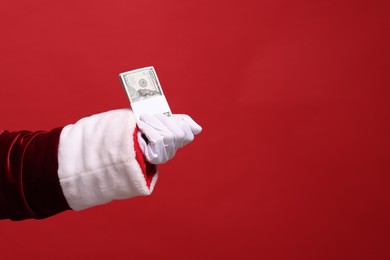 Photo of Santa Claus with dollar banknotes on red background, closeup. Space for text