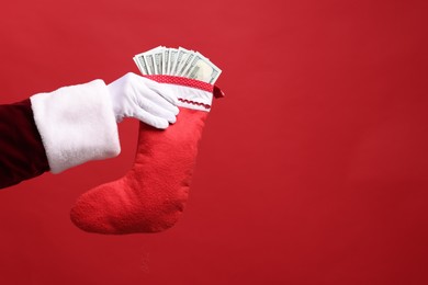 Photo of Santa Claus holding stocking with dollar banknotes on red background, closeup. Space for text