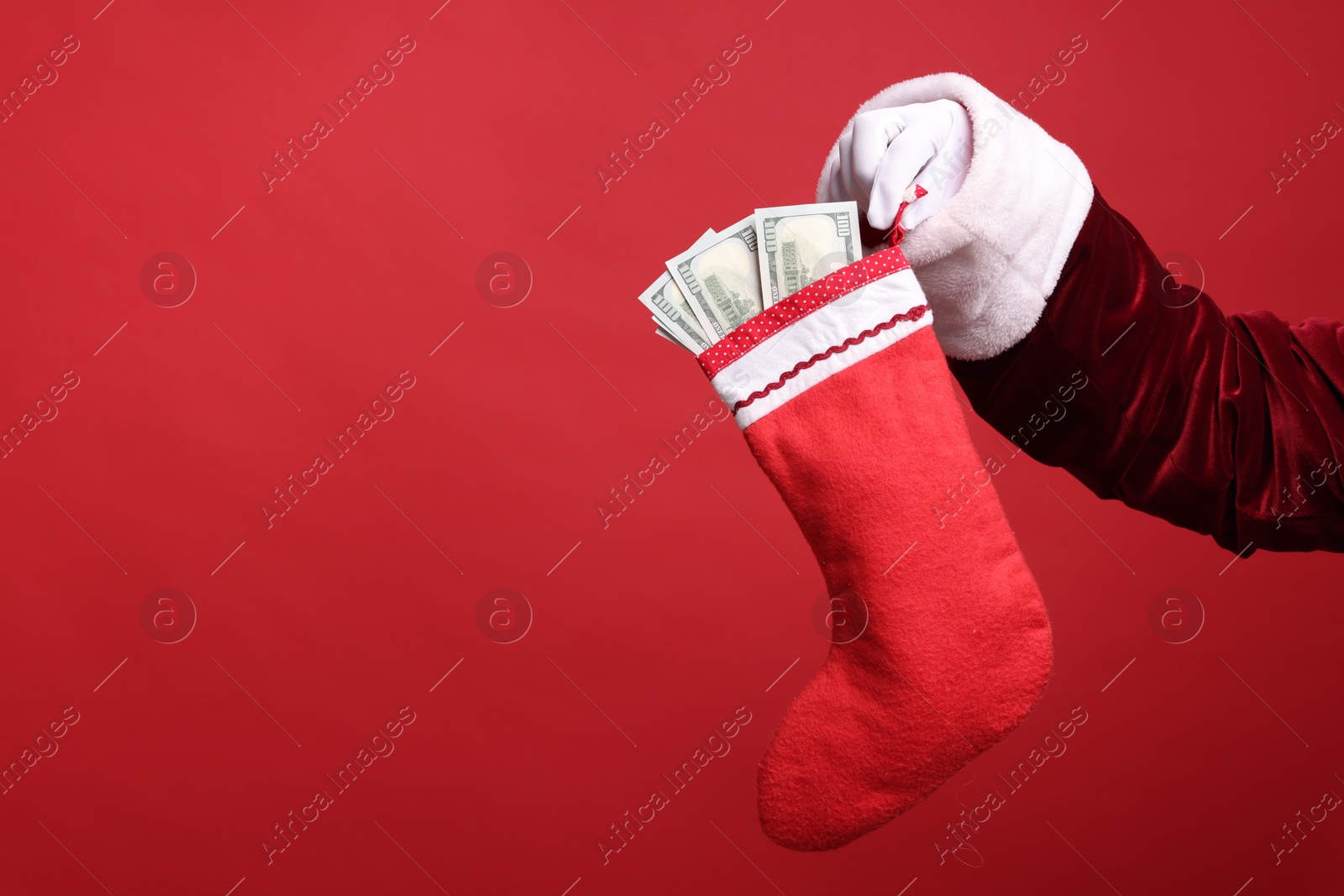 Photo of Santa Claus holding stocking with dollar banknotes on red background, closeup. Space for text