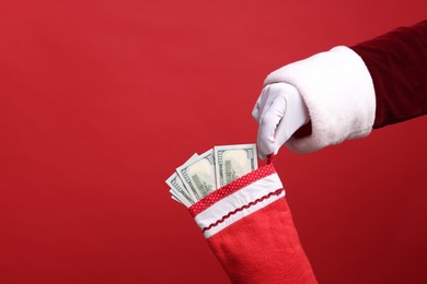 Photo of Santa Claus holding stocking with dollar banknotes on red background, closeup. Space for text