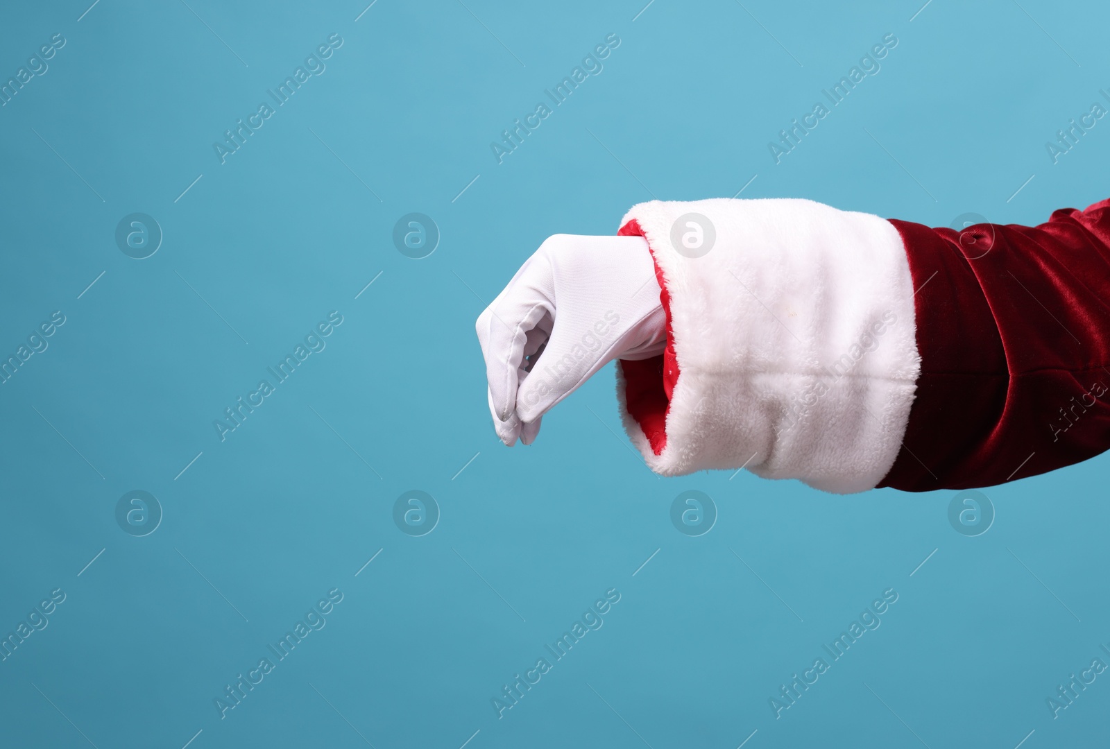 Photo of Santa Claus holding something on light blue background, closeup. Space for text