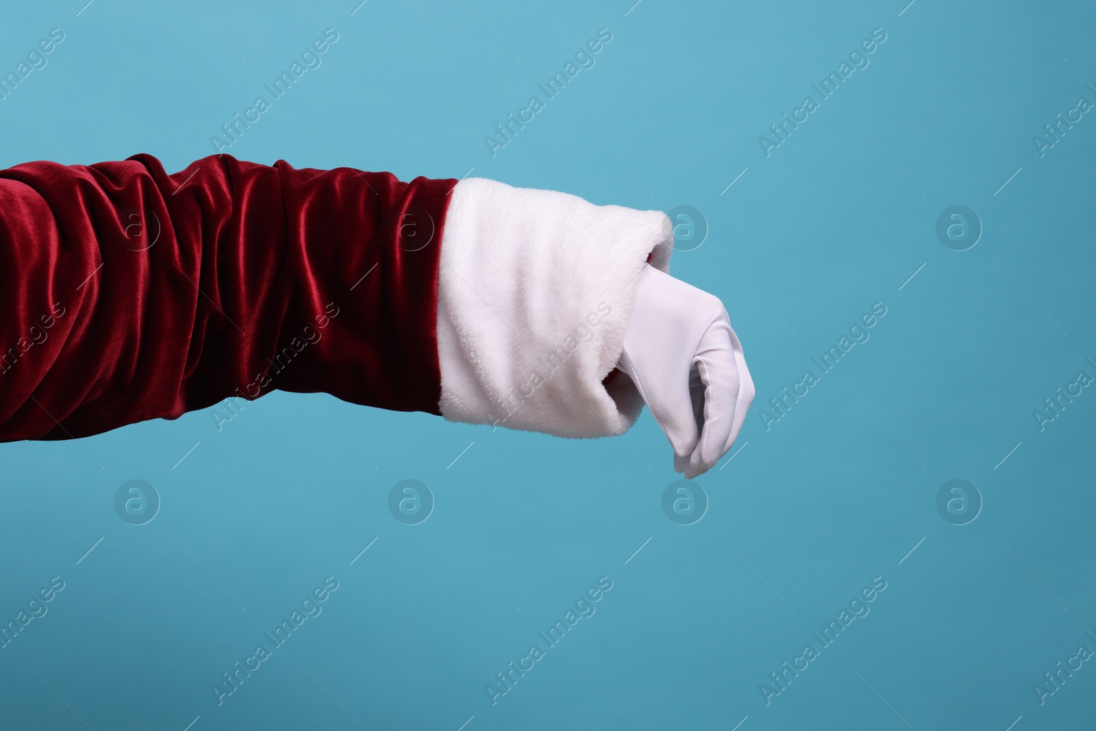 Photo of Santa Claus holding something on light blue background, closeup. Space for text