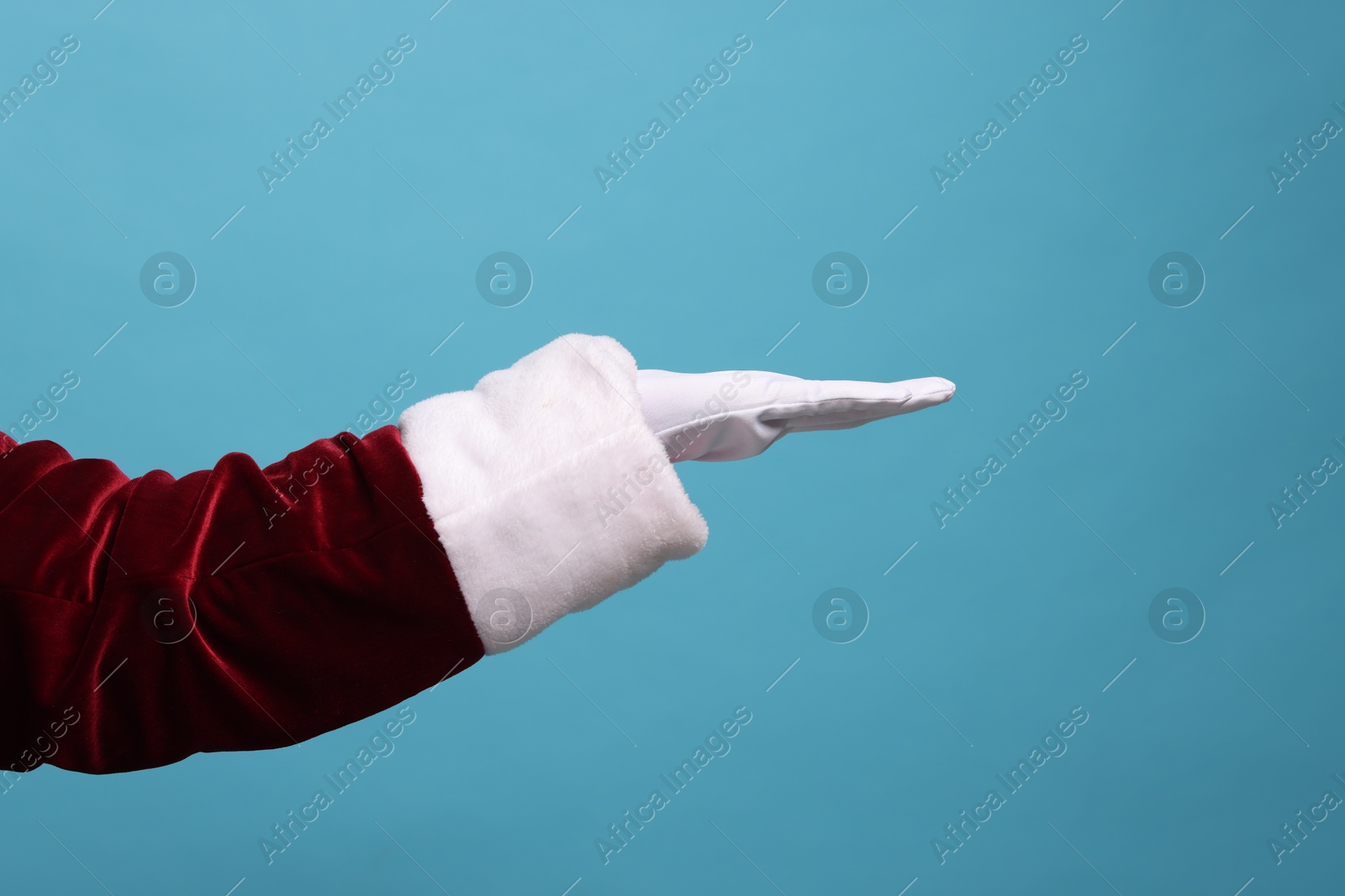 Photo of Santa Claus holding something on light blue background, closeup. Space for text