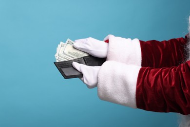 Photo of Santa Claus with dollar banknotes on light blue background, closeup