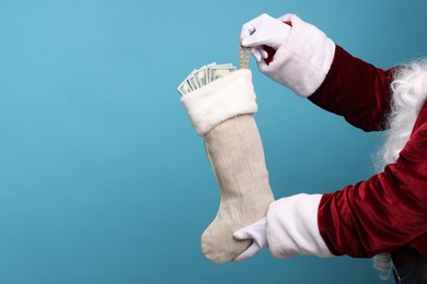 Photo of Santa Claus holding stocking with dollar banknotes on light blue background, closeup. Space for text