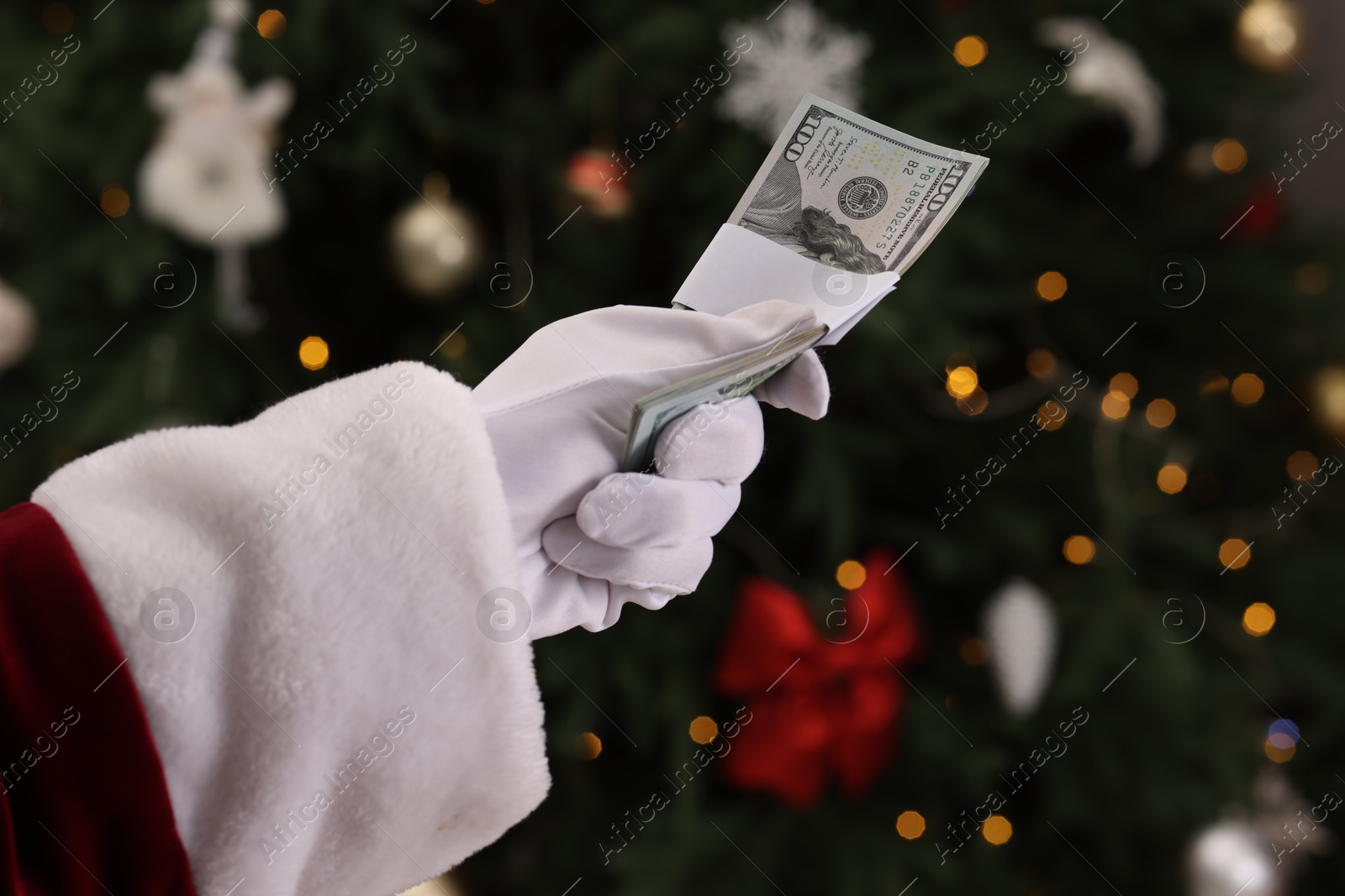 Photo of Santa Claus with dollar banknotes near Christmas tree indoors, closeup