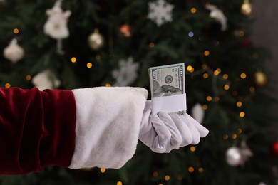 Photo of Santa Claus with dollar banknotes near Christmas tree indoors, closeup