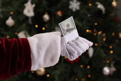 Photo of Santa Claus with dollar banknotes near Christmas tree indoors, closeup