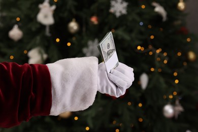 Photo of Santa Claus with dollar banknotes near Christmas tree indoors, closeup