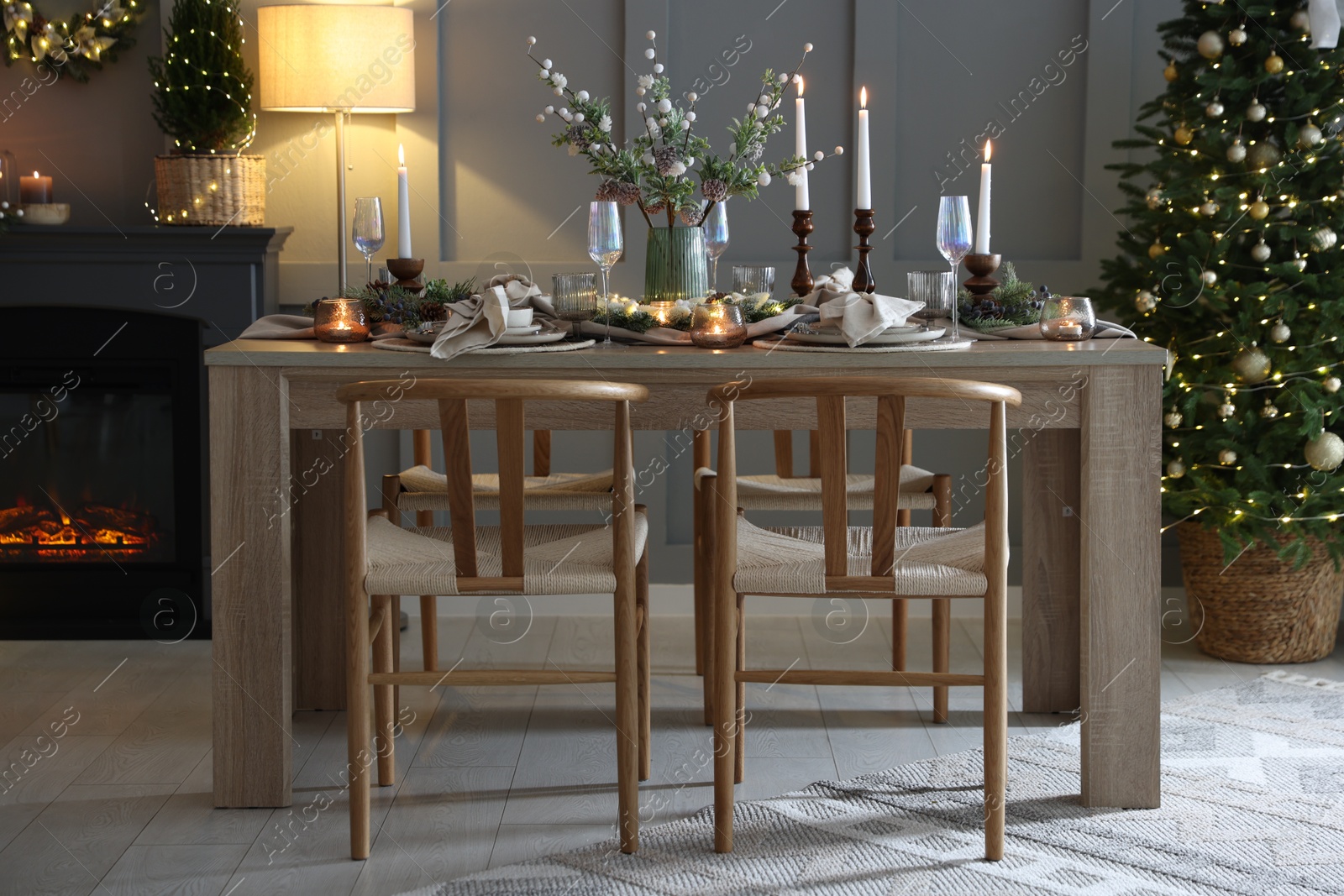 Photo of Christmas table setting with stylish dishware, glasses and burning candles in festive decorated room