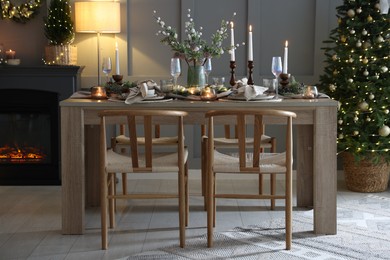 Photo of Christmas table setting with stylish dishware, glasses and burning candles in festive decorated room