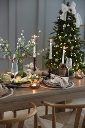 Photo of Christmas table setting with stylish dishware, glasses and burning candles in festive decorated room