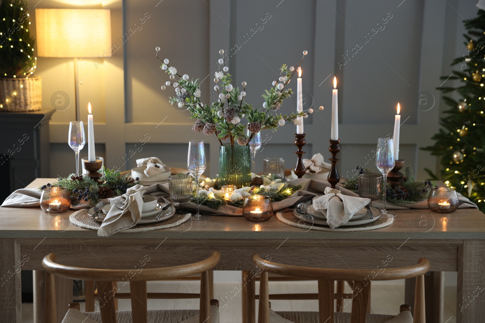 Photo of Christmas table setting with stylish dishware, glasses and burning candles in festive decorated room