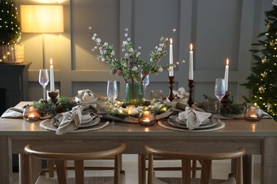 Photo of Christmas table setting with stylish dishware, glasses and burning candles in festive decorated room