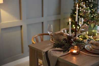 Photo of Christmas celebration. Festive table setting with dishware, glasses and decor in room