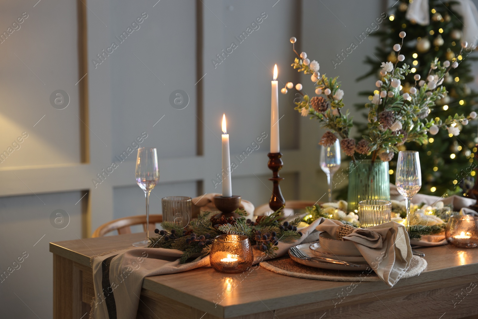 Photo of Christmas table setting with stylish dishware, glasses and burning candles in festive decorated room