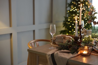 Photo of Christmas table setting with stylish dishware, glasses and burning candles in festive decorated room